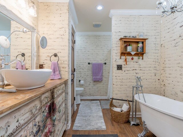 bathroom featuring brick wall, hardwood / wood-style floors, a tub to relax in, vanity, and toilet