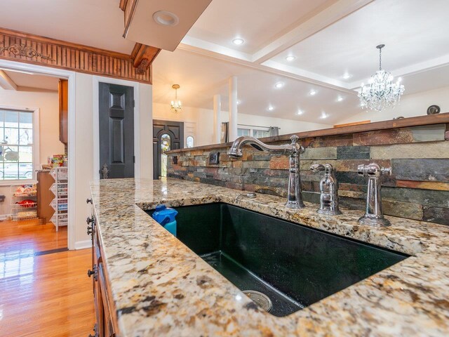 kitchen featuring sink, a notable chandelier, lofted ceiling with beams, light hardwood / wood-style floors, and decorative light fixtures