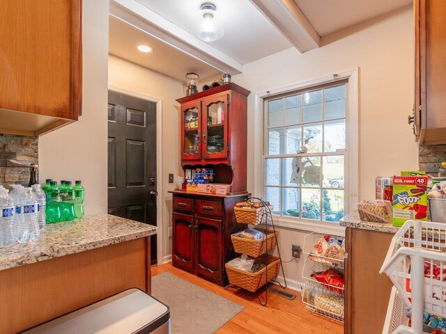 kitchen featuring backsplash, beam ceiling, light stone countertops, and light wood-type flooring