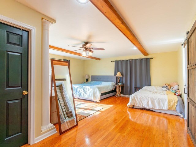 bedroom with beamed ceiling, ceiling fan, a barn door, and hardwood / wood-style flooring