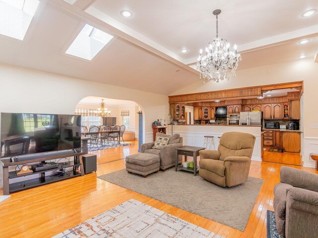 living room featuring an inviting chandelier, lofted ceiling with skylight, and light wood-type flooring