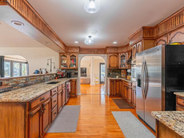 kitchen with sink, tasteful backsplash, light hardwood / wood-style flooring, stainless steel appliances, and light stone countertops