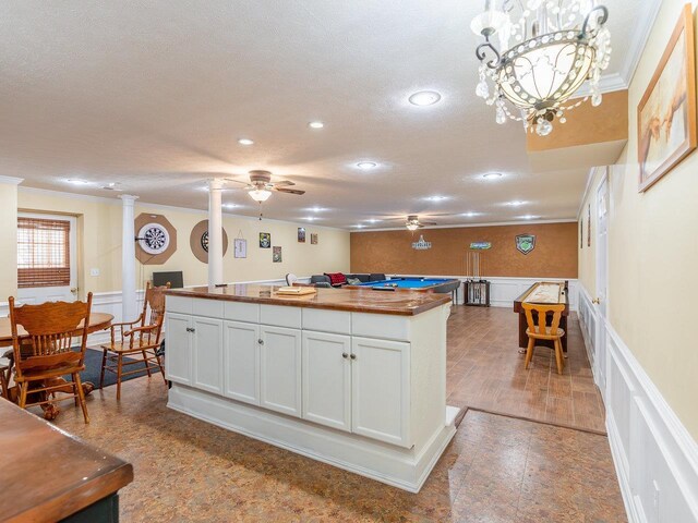 kitchen with crown molding, wooden counters, white cabinetry, a kitchen island, and decorative light fixtures