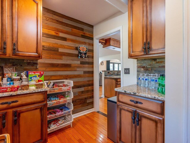 kitchen featuring tasteful backsplash, light stone countertops, light hardwood / wood-style floors, and wood walls