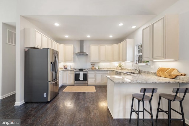 kitchen with a sink, stainless steel appliances, a peninsula, wall chimney range hood, and light stone countertops