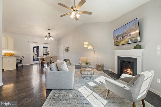 living area with baseboards, dark wood finished floors, lofted ceiling, ceiling fan with notable chandelier, and a glass covered fireplace