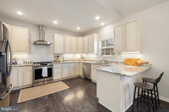 kitchen with light stone counters, appliances with stainless steel finishes, a peninsula, dark wood-style floors, and wall chimney exhaust hood