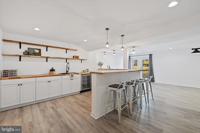 kitchen with a sink, wine cooler, butcher block countertops, white cabinetry, and open shelves