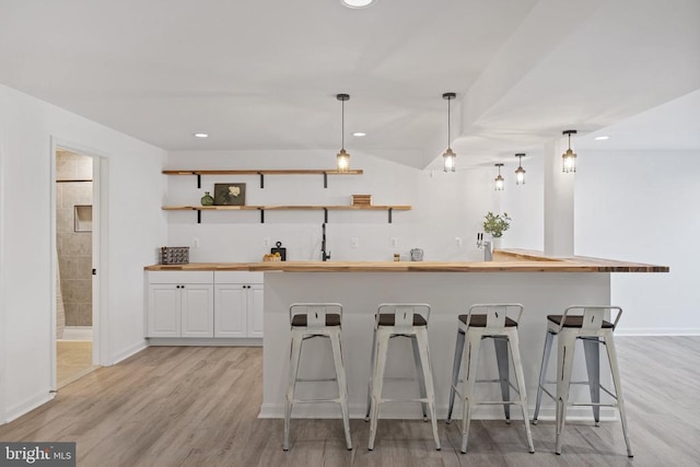 kitchen with a breakfast bar area, open shelves, butcher block countertops, light wood-style floors, and white cabinetry