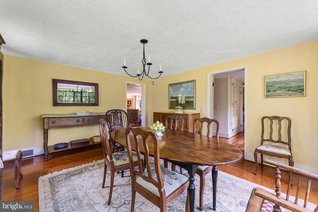 dining area with an inviting chandelier, a textured ceiling, baseboards, wood finished floors, and visible vents