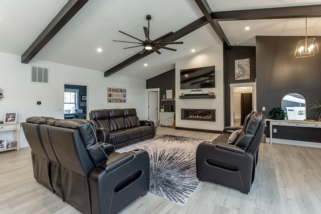 living room featuring ceiling fan with notable chandelier, high vaulted ceiling, beamed ceiling, a large fireplace, and light wood-type flooring