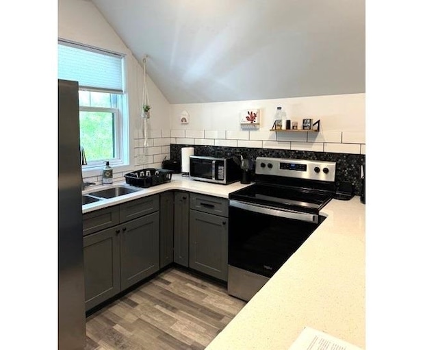 kitchen with gray cabinets, backsplash, stainless steel appliances, wood-type flooring, and vaulted ceiling