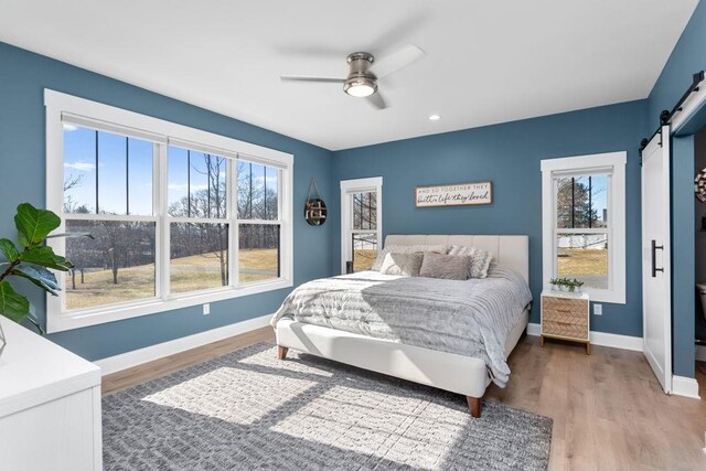 bedroom featuring ceiling fan, a barn door, and light hardwood / wood-style floors