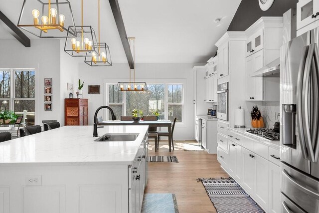 kitchen with sink, appliances with stainless steel finishes, pendant lighting, a large island, and wall chimney range hood