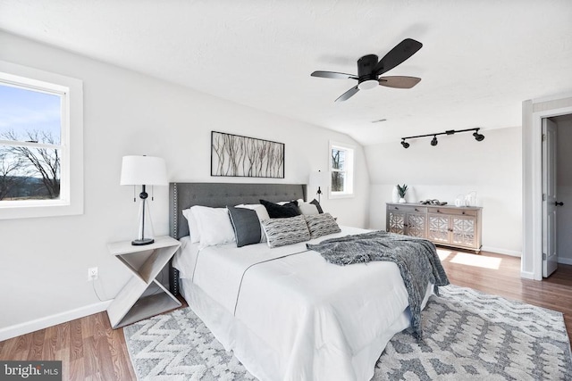 bedroom with ceiling fan, wood-type flooring, rail lighting, and vaulted ceiling