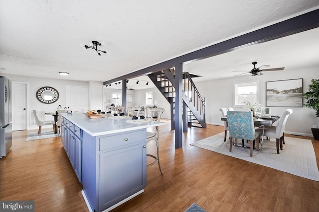 kitchen with blue cabinetry, a kitchen bar, wood-type flooring, stainless steel refrigerator, and a kitchen island