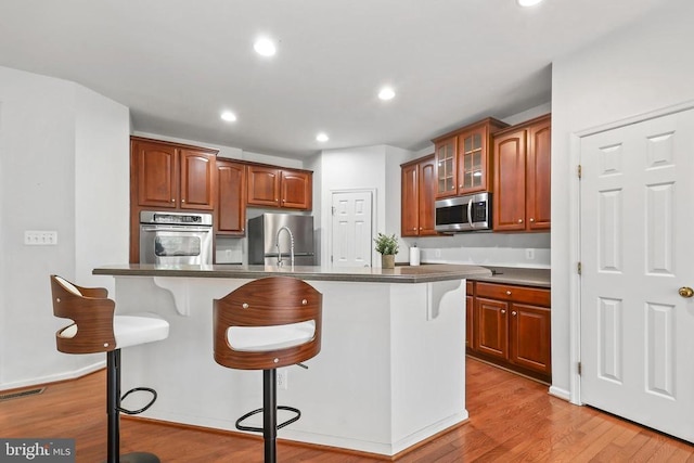 kitchen featuring visible vents, glass insert cabinets, appliances with stainless steel finishes, light wood-style floors, and a kitchen bar