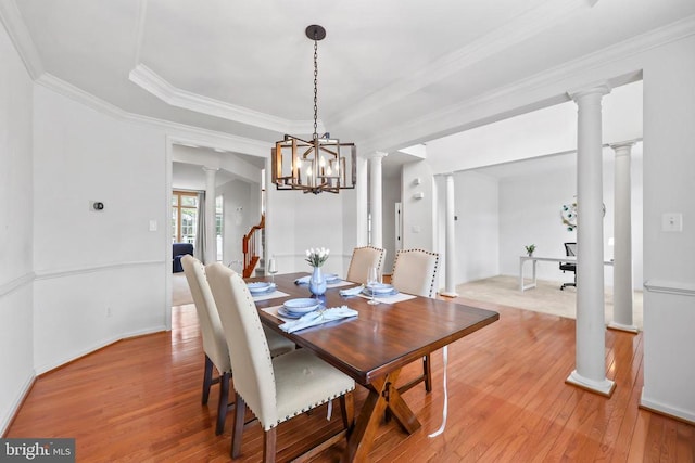 dining room with ornamental molding, a tray ceiling, light wood finished floors, and ornate columns