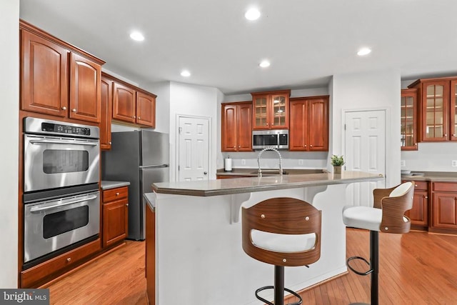 kitchen featuring a breakfast bar area, stainless steel appliances, light wood-style floors, glass insert cabinets, and a sink