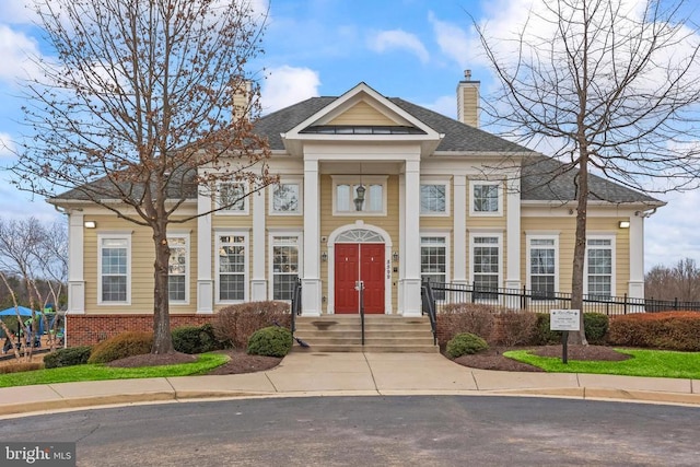 neoclassical / greek revival house with brick siding, fence, a chimney, and roof with shingles