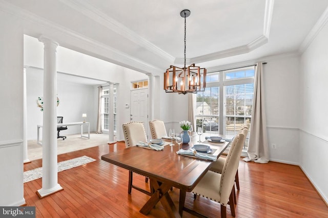 dining room featuring decorative columns, a raised ceiling, light wood-style flooring, ornamental molding, and a chandelier