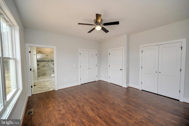 unfurnished bedroom with visible vents, two closets, dark wood finished floors, and baseboards