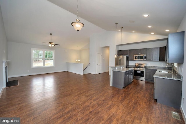 kitchen featuring stainless steel appliances, a sink, a kitchen island, open floor plan, and decorative light fixtures