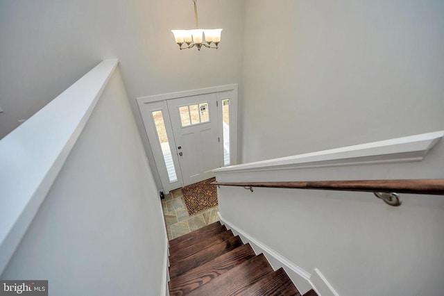 foyer entrance with stairs, stone finish flooring, baseboards, and a notable chandelier