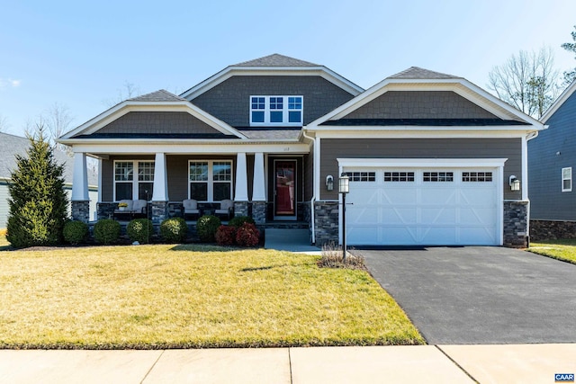 craftsman-style house with an attached garage, a porch, a front yard, stone siding, and driveway