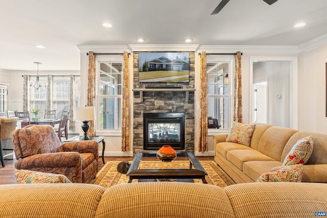 living room featuring wood finished floors, recessed lighting, a stone fireplace, crown molding, and ceiling fan