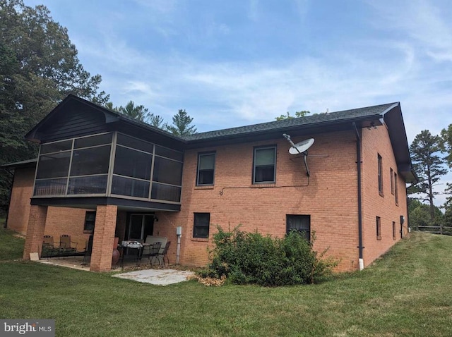 rear view of property with brick siding, a lawn, a patio area, and a sunroom