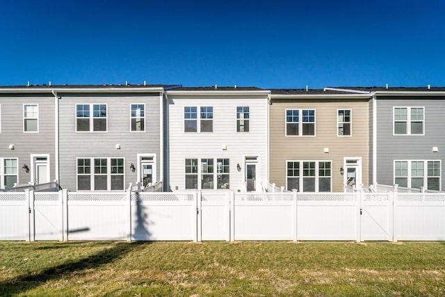 back of house featuring a lawn, a fenced backyard, and a gate