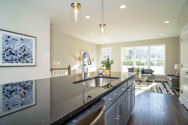 kitchen featuring dark wood-type flooring, decorative light fixtures, dishwasher, dark stone countertops, and a sink