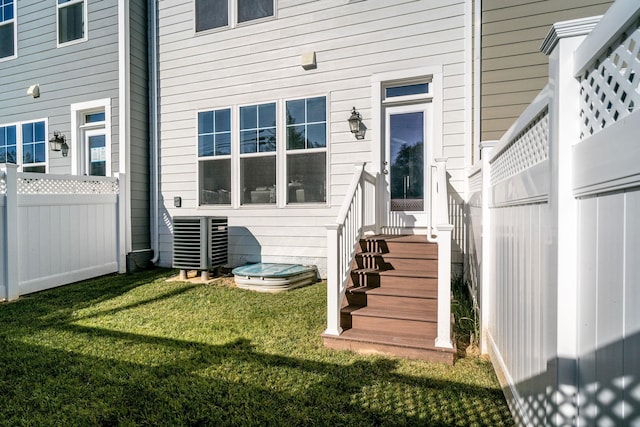entrance to property featuring central air condition unit, a yard, and fence