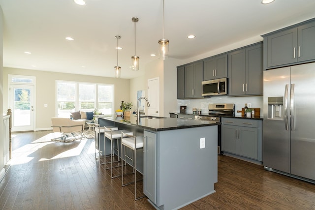 kitchen with a kitchen bar, decorative backsplash, gray cabinets, stainless steel appliances, and a sink
