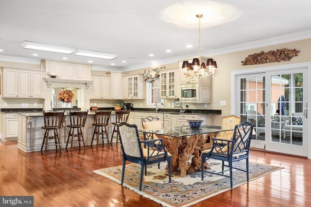 dining space featuring an inviting chandelier, sink, crown molding, and hardwood / wood-style flooring