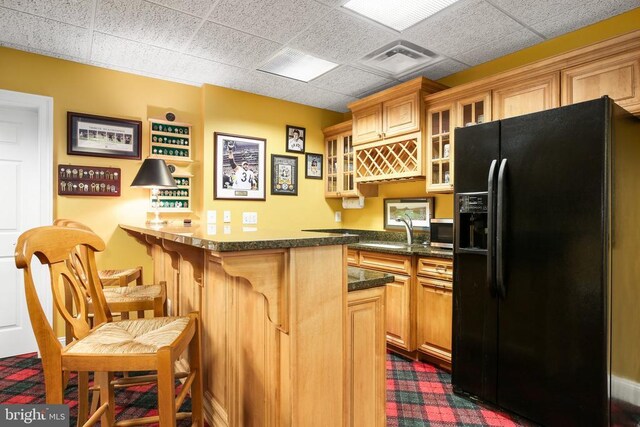 kitchen with sink, a breakfast bar area, black fridge, a drop ceiling, and kitchen peninsula