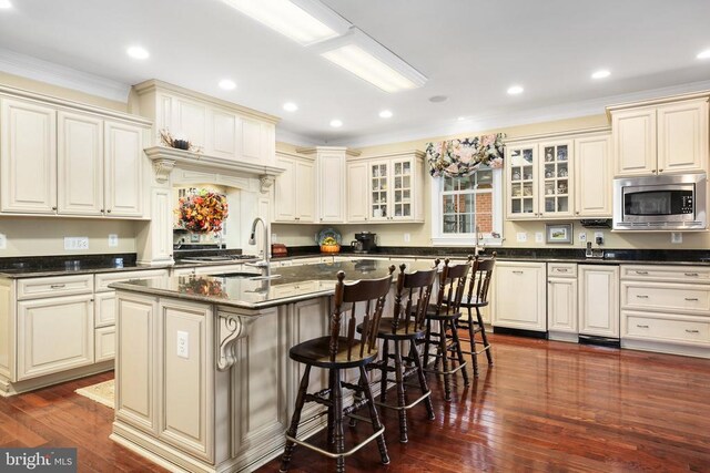 kitchen featuring stainless steel microwave, cream cabinets, dark hardwood / wood-style floors, and an island with sink