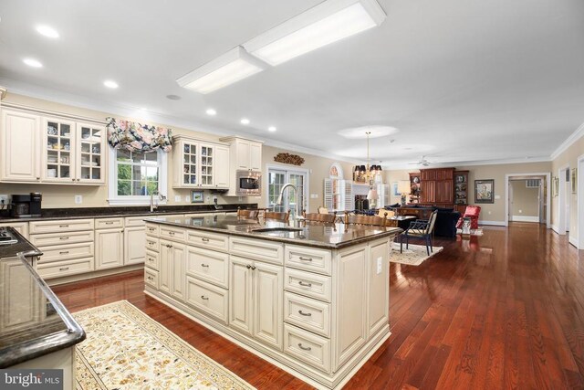 kitchen featuring stainless steel microwave, cream cabinets, a kitchen island with sink, and sink