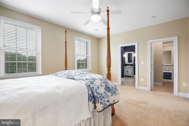 bedroom with ensuite bathroom, light colored carpet, and ceiling fan