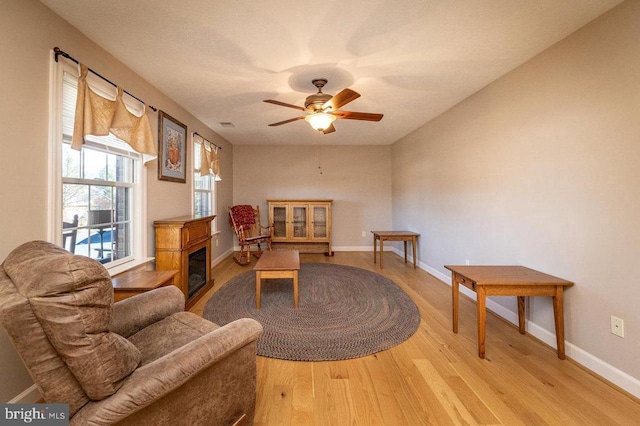 interior space featuring light wood-style flooring, baseboards, a ceiling fan, and a glass covered fireplace