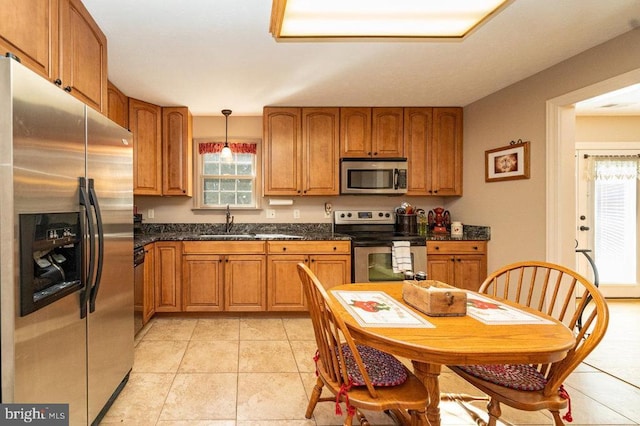 kitchen featuring brown cabinetry, light tile patterned floors, stainless steel appliances, and a sink