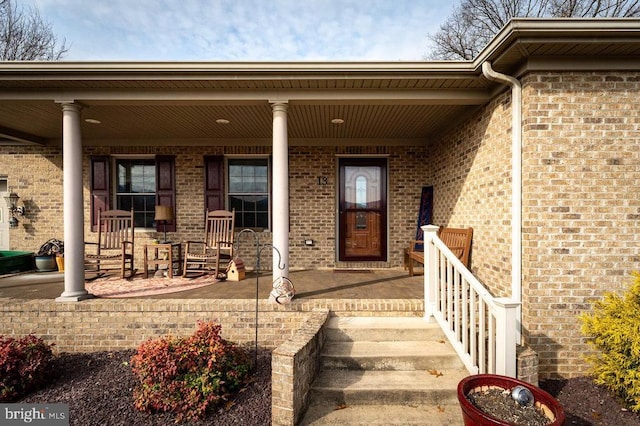 doorway to property with covered porch and brick siding