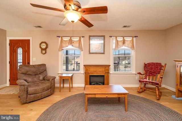 living area with a fireplace, wood finished floors, visible vents, and baseboards