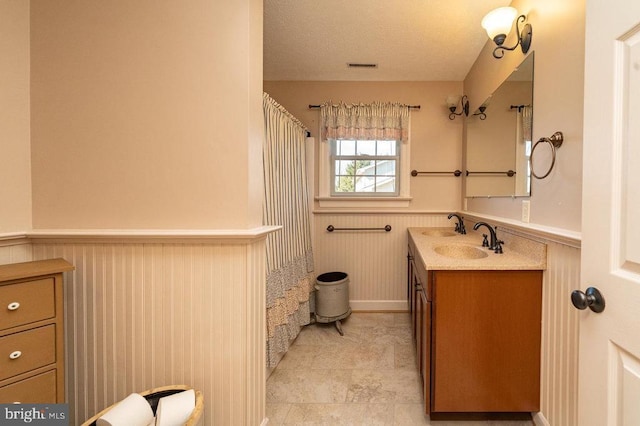 bathroom with visible vents, a wainscoted wall, vanity, and a textured ceiling