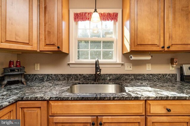 kitchen featuring brown cabinetry, a sink, and dark stone countertops