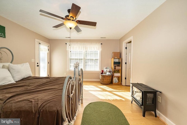 bedroom featuring ceiling fan, light wood-type flooring, a wood stove, and baseboards