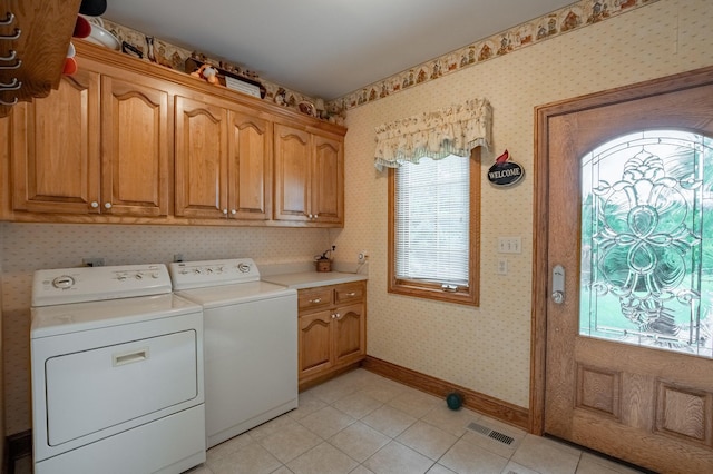 clothes washing area with cabinets, light tile patterned floors, and washer and clothes dryer