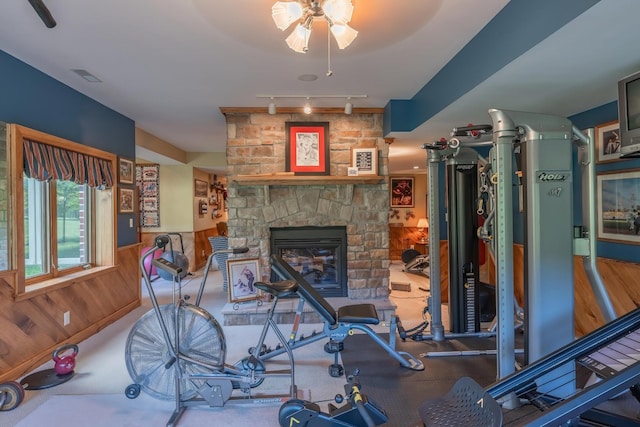 workout area with a stone fireplace, track lighting, and wood walls