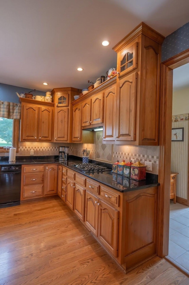 kitchen with stainless steel gas cooktop, light hardwood / wood-style flooring, dark stone countertops, dishwasher, and decorative backsplash